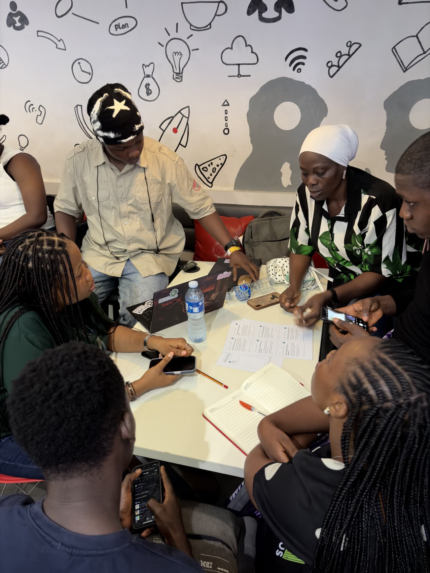 A team leaning over the printed design canvas, with laptops and notebooks open